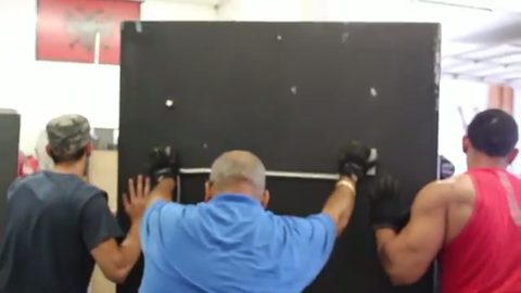 three movers push a large heavy steel safe against a wall