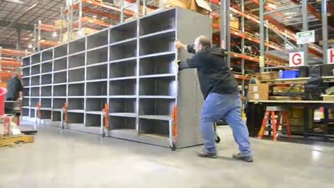 worker pushing a large steel industrial shelving unit on casters