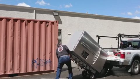 man pushing a stainless refrigerator on a hand truck up into a pickup bed